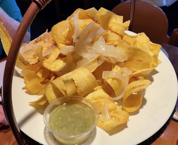 A white plate piled high with plantain chips and a glass with mojito.