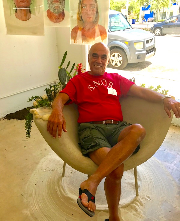A man in shorts and a red t-shirt sitting in a chair made of concrete