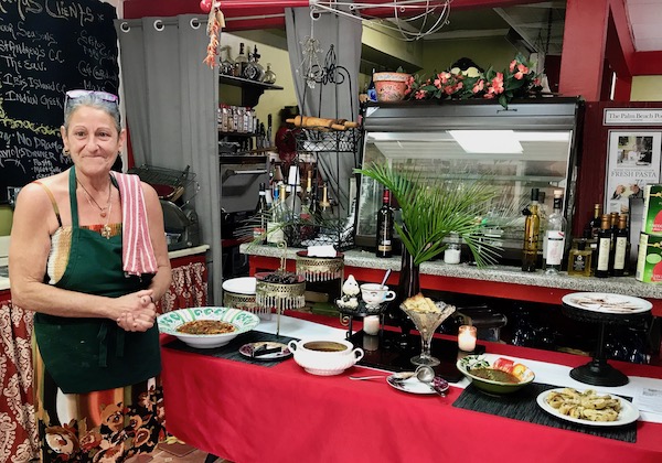 A woman in a black apron standing next to a buffet table filled with food