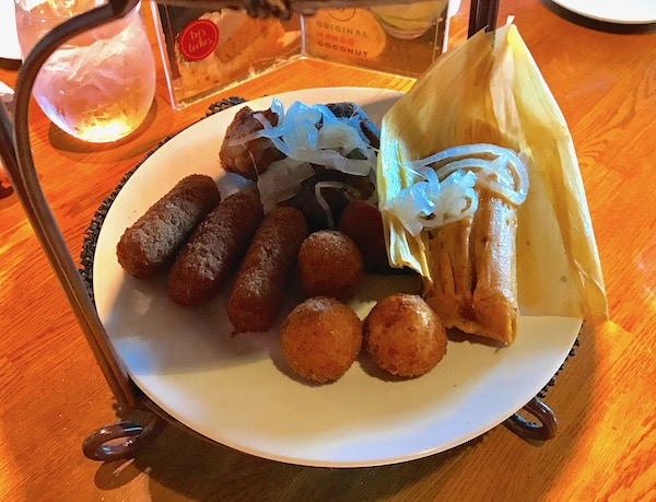 A white plate on a wood table. Plate has assorted appetizers on it.