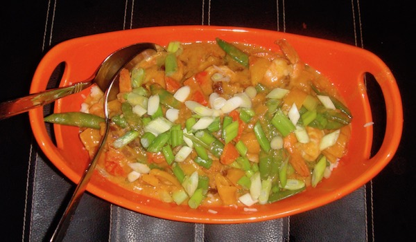 Oval orange serving dish containing shrimp., rice, colored peppers and scallions