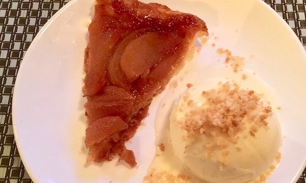 A white plate with a wedge of an apple tart on the left with a scoop of white ice cream next to it on the right.