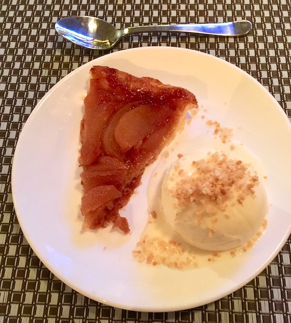 A white plate with a wedge of an apple tart on the left with a scoop of white ice cream next to it on the right.