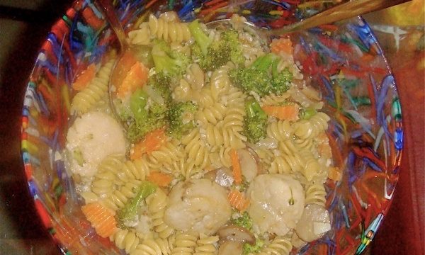 Red, blue, green and yellow glass bowl filled with penne pasta, broccoli, carrots and scallops in gorgonzola sauce