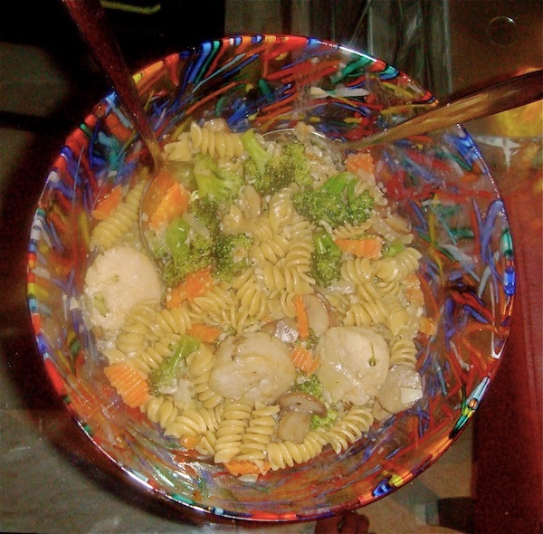 Red, blue, green and yellow glass bowl filled with penne pasta, broccoli, carrots and scallops in gorgonzola sauce