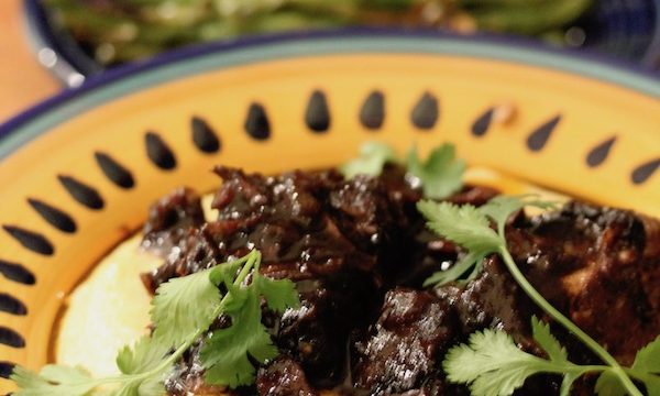 Yellow and blue pasta bowl filled with polenta and topped with braised short ribs and a dish of asparagus in the background