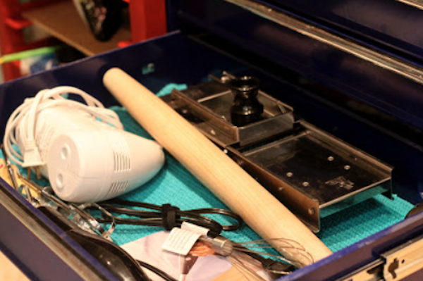 A drawer filled with a hand mixer, rolling pin and mandoline