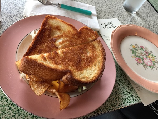 A grilled sandwich with chips inside on a pink plate with another plate to the right.