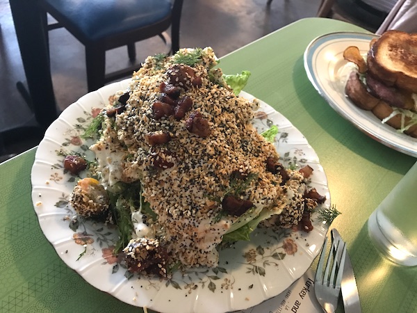 A white plate with a huge wedge of iceberg lettuce covered with bacon, dressing and everything bagel spice.