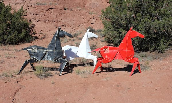 A black, a red and a white horse sculptures sitting on dirt path