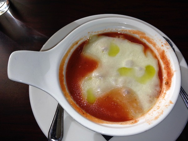 A white crock filled with tomato soup and melted cheese