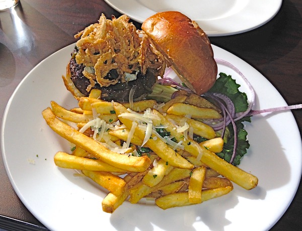 A white plate with fries and a burger topped with fried onion straws