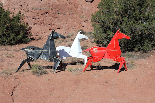 A black, a red and a white horse sculptures sitting on dirt path