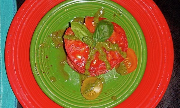 Large red dinner plate with olive green salad plate on top filled with slices of red tomato, fresh basil and mozzarella