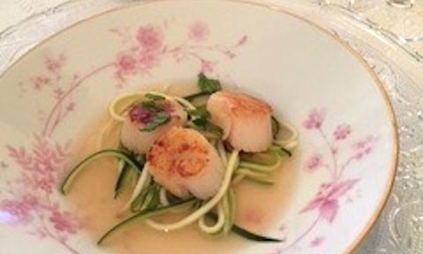 A white soup plate with pink flowers filled with Seared Scallops with Tomato Consommé and Julienne of Courgette