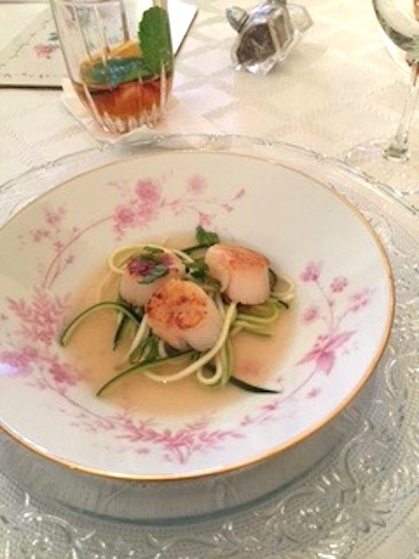 A white soup plate with pink flowers filled with Seared Scallops with Tomato Consommé and Julienne of Courgette