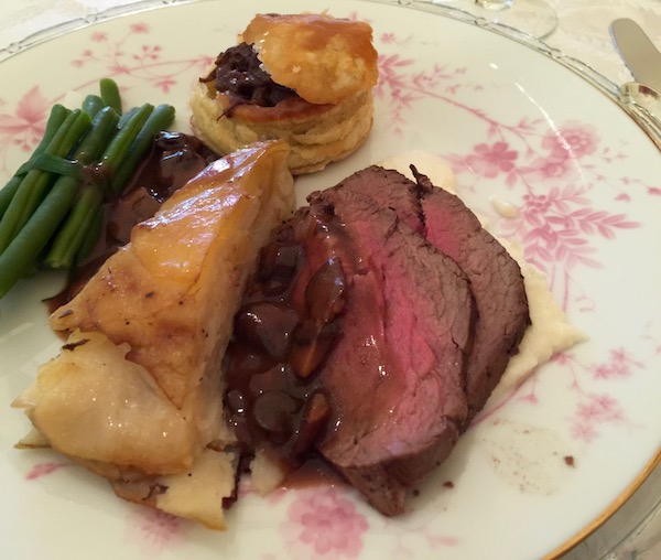 A white plate with pink flowers topped with Beef in a Basket with Sliced Filet, Creamed Cauliflower, French Green Beans and Potatoes Anna
