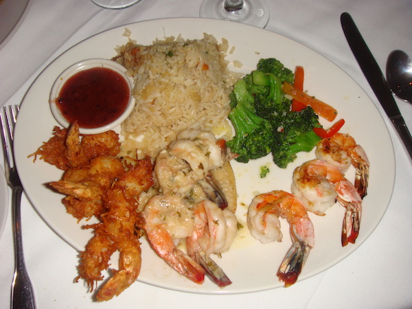 White dinner plate filled with 3 different shrimp preparations, rice, broccoli and sauce