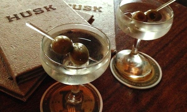 A wood table with 2 Husk menus and 2 martinis with olives