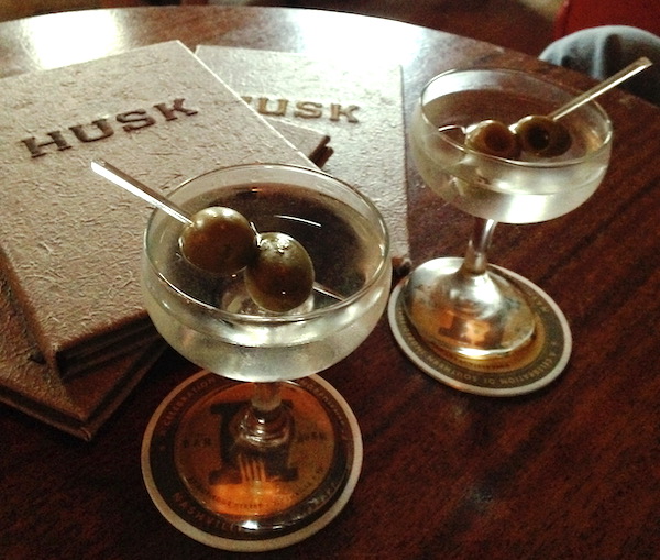 A wood table with 2 Husk menus and 2 martinis with olives