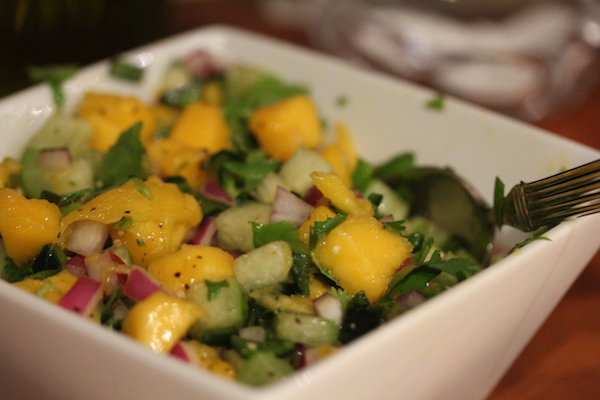 A white square bowl filled with chopped mangoes, tomatillos and red onion