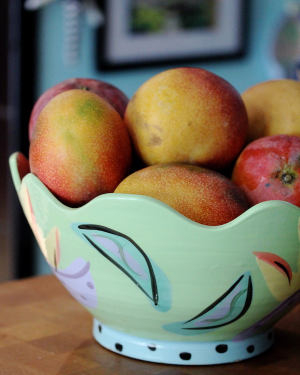 An aqua ceramic bowl filled with ripe mangoes