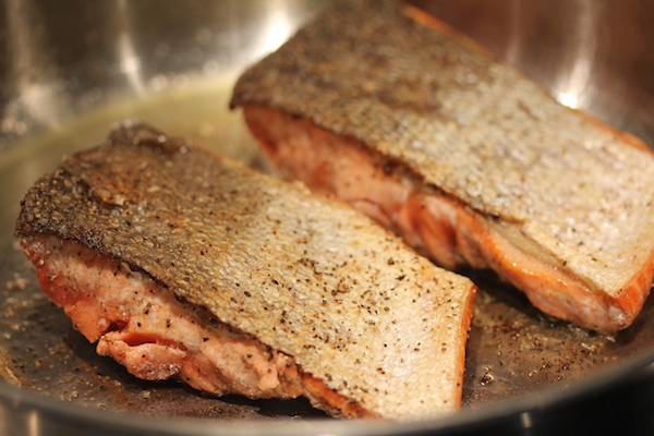 A sauté pan with two skin on salmon filets searing