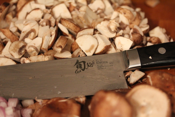 A whole pile of sliced mushrooms and a chef's knife.