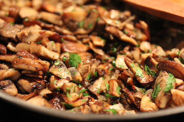 A sauté pan full of cooked sliced mushrooms and shallot speckled with parsley.