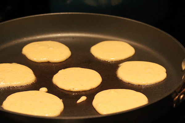 Anodized pan with small yellow pancakes cooking on first side