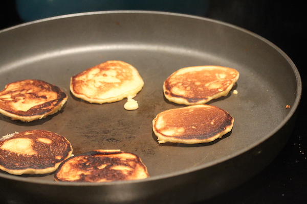 Anodized pan with small yellow pancakes cooking on second side