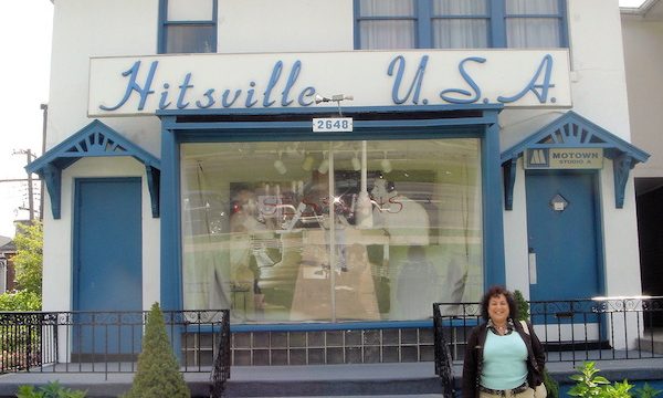A woman standing in front of the steps to a white building with blue trim and a sign reading Hitsville, USA