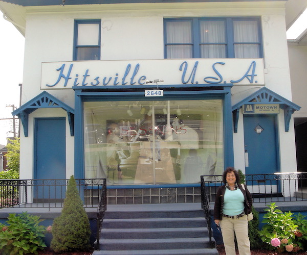A woman standing in front of the steps to a white building with blue trim and a sign reading Hitsville, USA