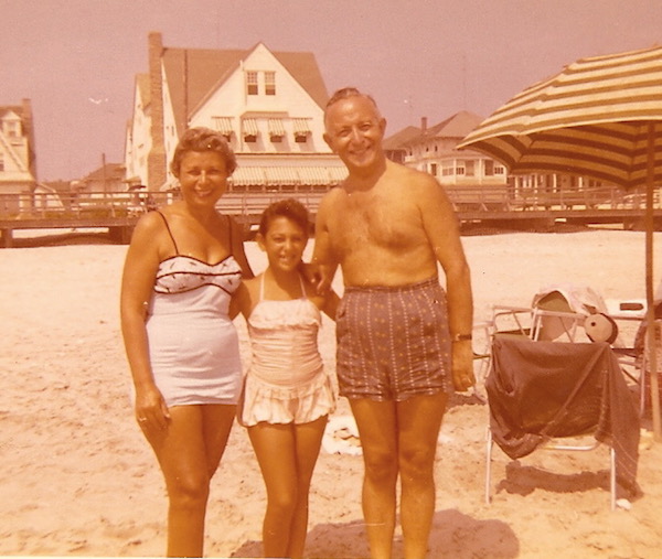 An older man and woman with their young granddaughter between them on the beach