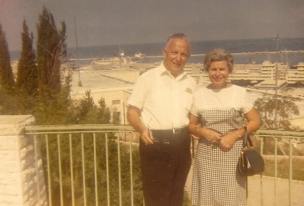 An older man and woman standing in from of a rail with beach and ocean behind them