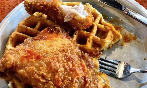 Fried Chicken on a round waffle drizzled with honey on a silver plate