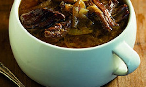 A mint green crock filled with onion and flanken soup on a wood surface.