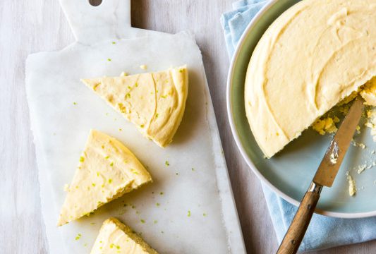 A partial Crustless Key Lime Cheesecake in a pan with 3 slices on a white cutting board.