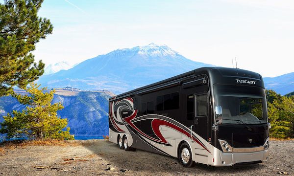 A black and tan Class A Hybrid Electric RV! with mountain in background.