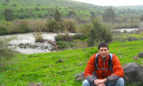 A man crouching with hills and water in the background seeing Israel by Foot.