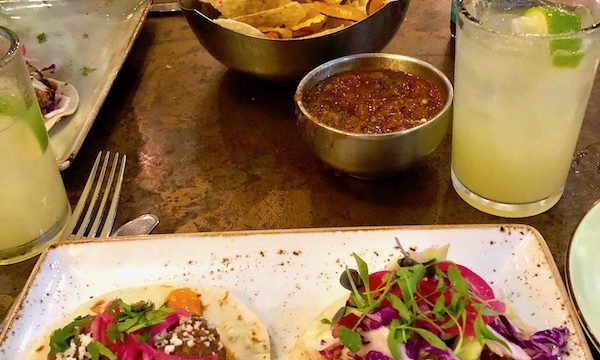 A wood table topped with a plate of tacos, salsa, chips and a margarita at Johnny Sanchez Mexican Restaurant