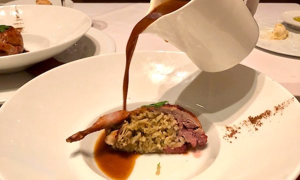 Soup being poured into a shallow white bowl containing a half a rice and andouille stuffed quail at Restaurant R'evolution NOLA