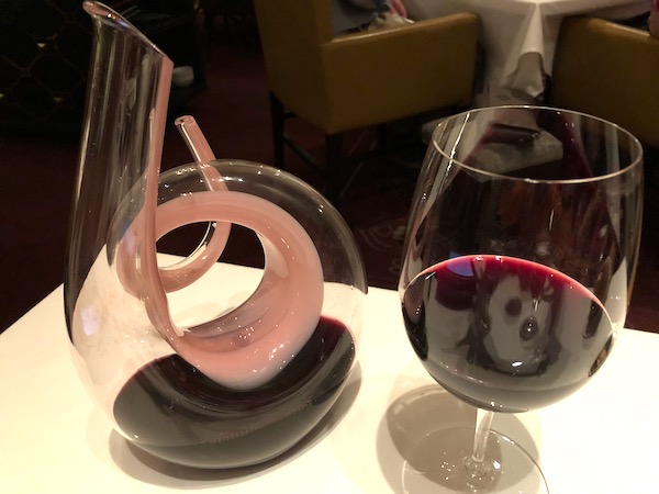 A spiral glass wine decanter with pink swirl next to a glass of red wine at Restaurant R'evolution NOLA.