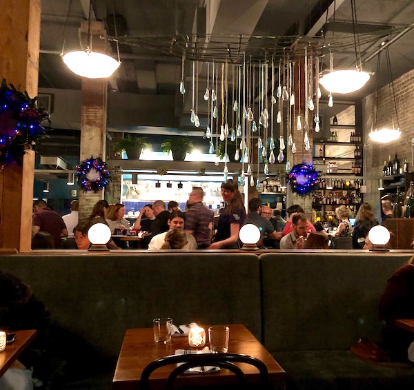 The view of the bar at Bywater American Bistro in New Orleans looking through a wall of hanging glass pendants.