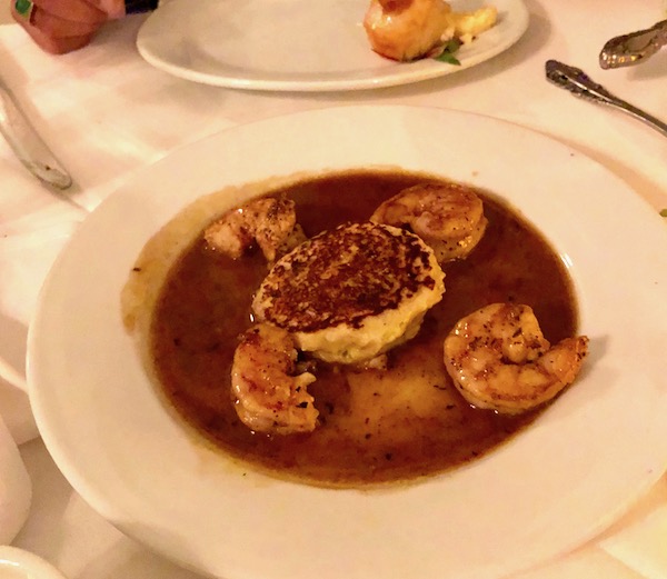A white bowl filled with BBQ shrimp, sauce and a rice fritter at Brigtsen's in New Orleans Revisited