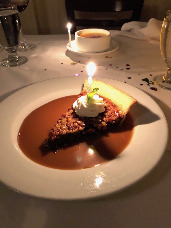 A slice of Pecan Pie with a lit candle in a pool of caramel sauce at Brigtsen's in New Orleans Revisited