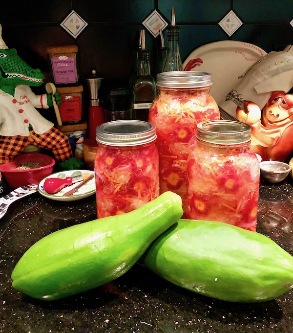 One large and two smaller mason jars of Green Papaya Salad with two papayas on a kitchen counter.