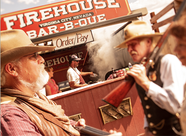 A man with a rifle in front of a sign that says Firehouse BBQ from 60 Years of Camel and Ostrich Racing!