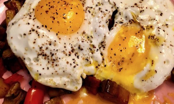 Andouille Hash with Fried Egg with one yolk oozing onto a pink plate.