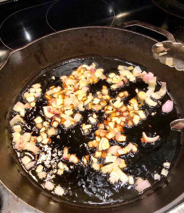A cast iron skillet with diced shallots cooking in oil for my Andouille Hash with Fried Egg.